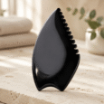 Black Wing Gua Sha Tool beside towels and facial oil